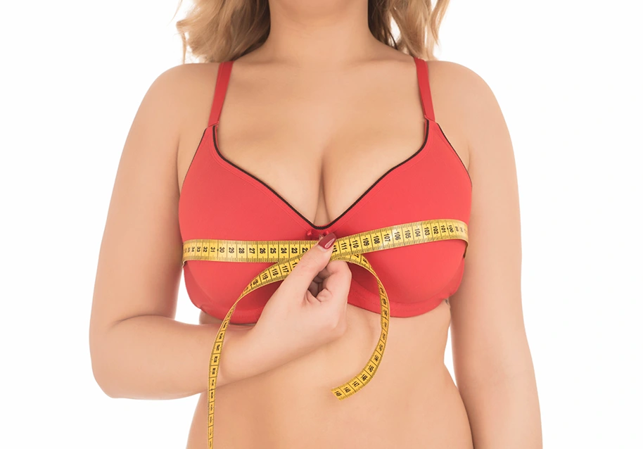 Woman measuring breast size with tape measure, representing breast reduction size options and consultation planning